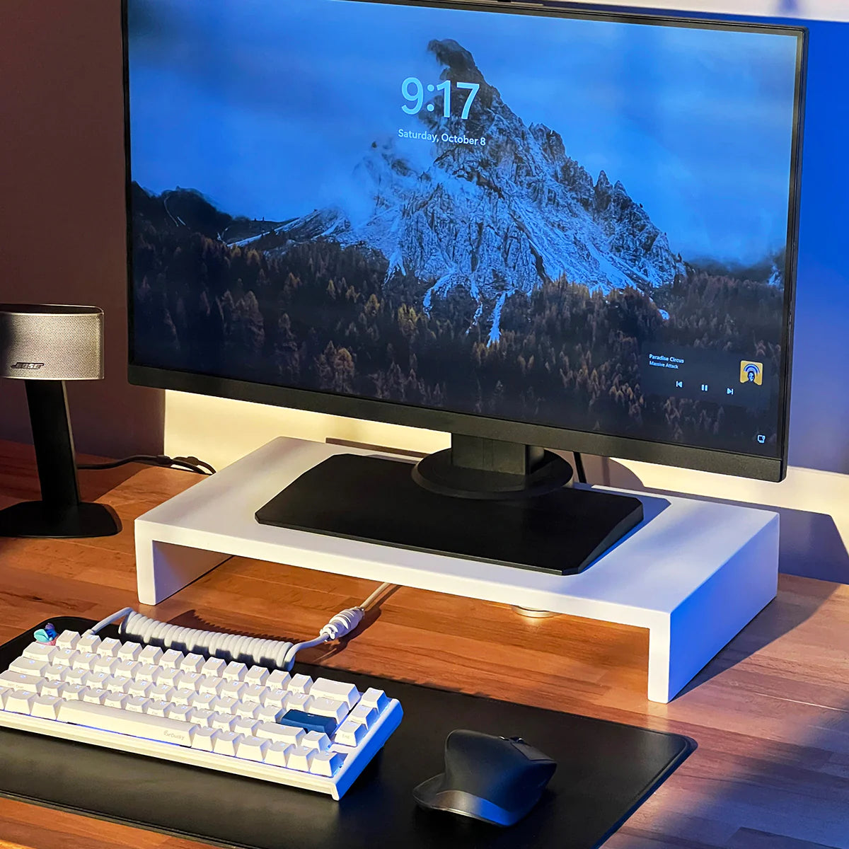 Modern stand riser by woodsy desk setup with monitor, mechanical keyboard, and ergonomic mouse on a wooden table.