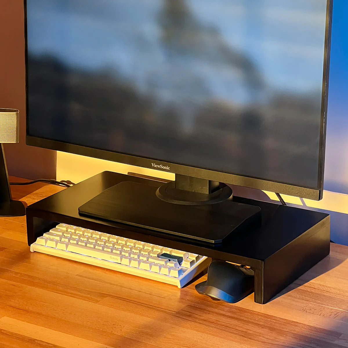 Monitor on stand riser by woodsy with mechanical keyboard and mouse on wooden desk, home office setup.