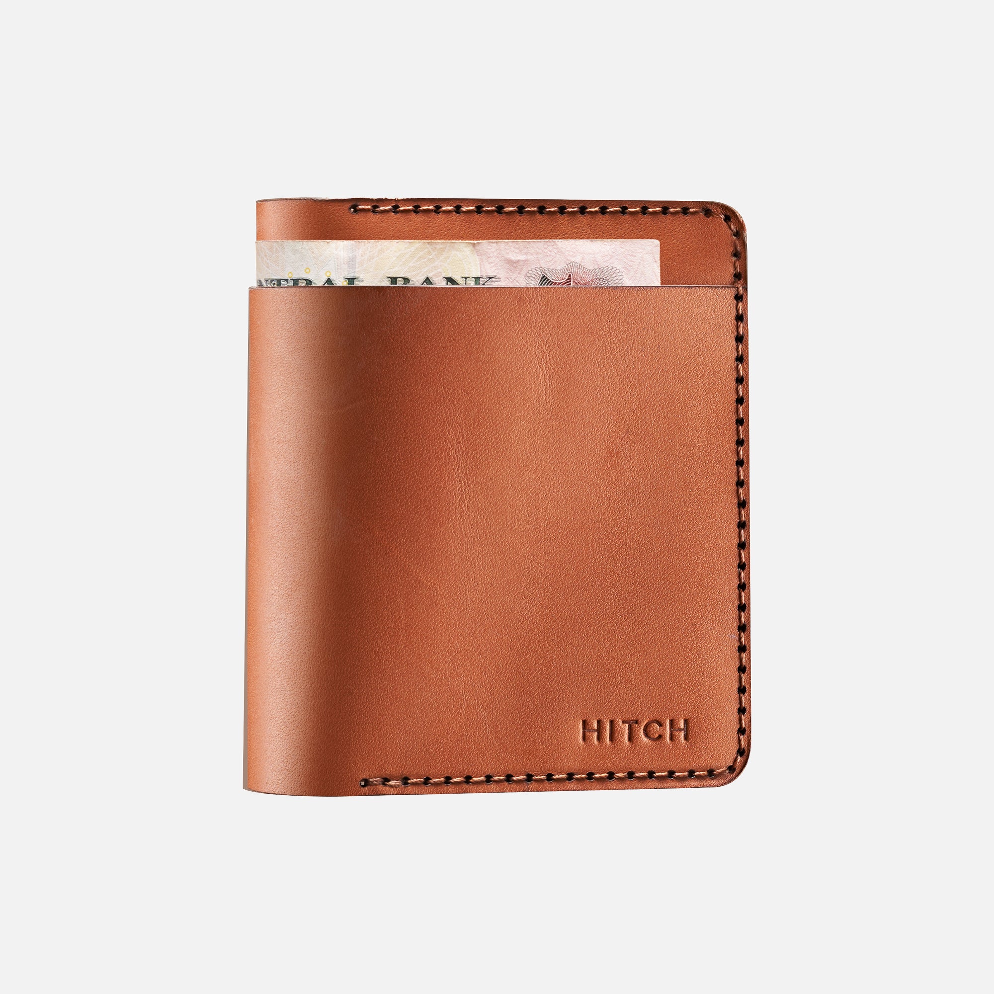 Brown leather minimalist bifold wallet with stitched detailing and currency peeking out.