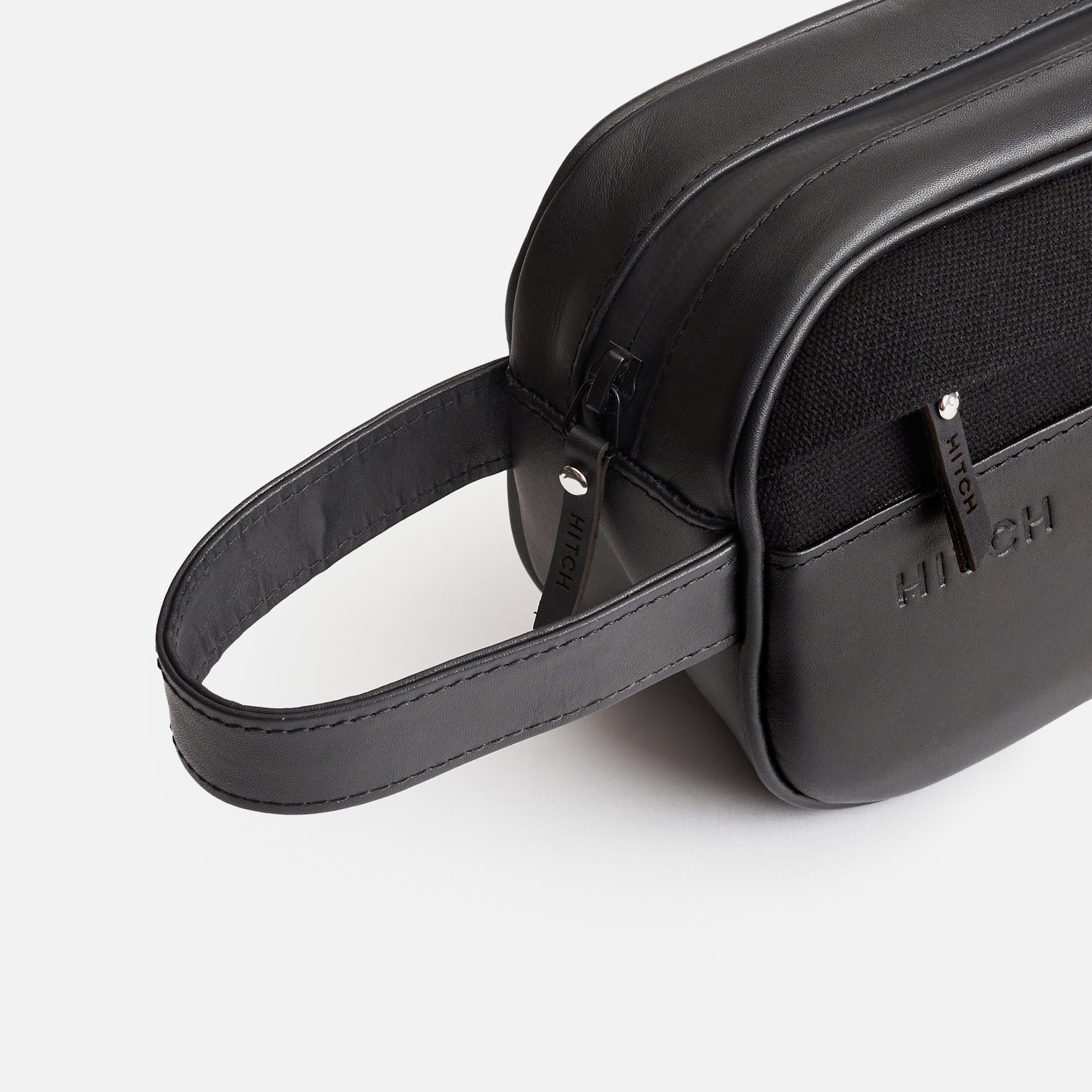 Black leather designer dopp kit with embossed "HITCH" logo and wrist strap on a white background.