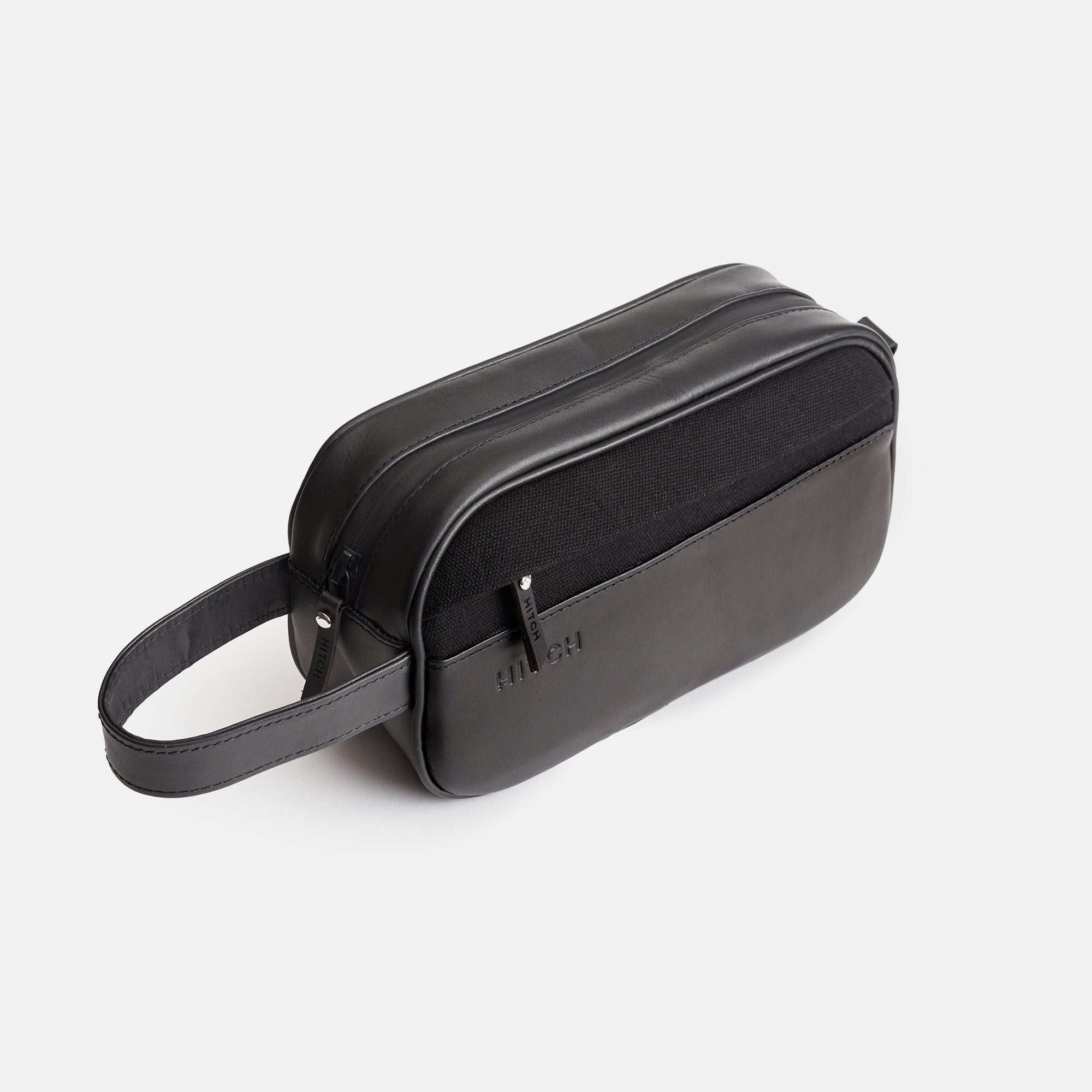 Black leather dopp kit with wrist strap on white background.