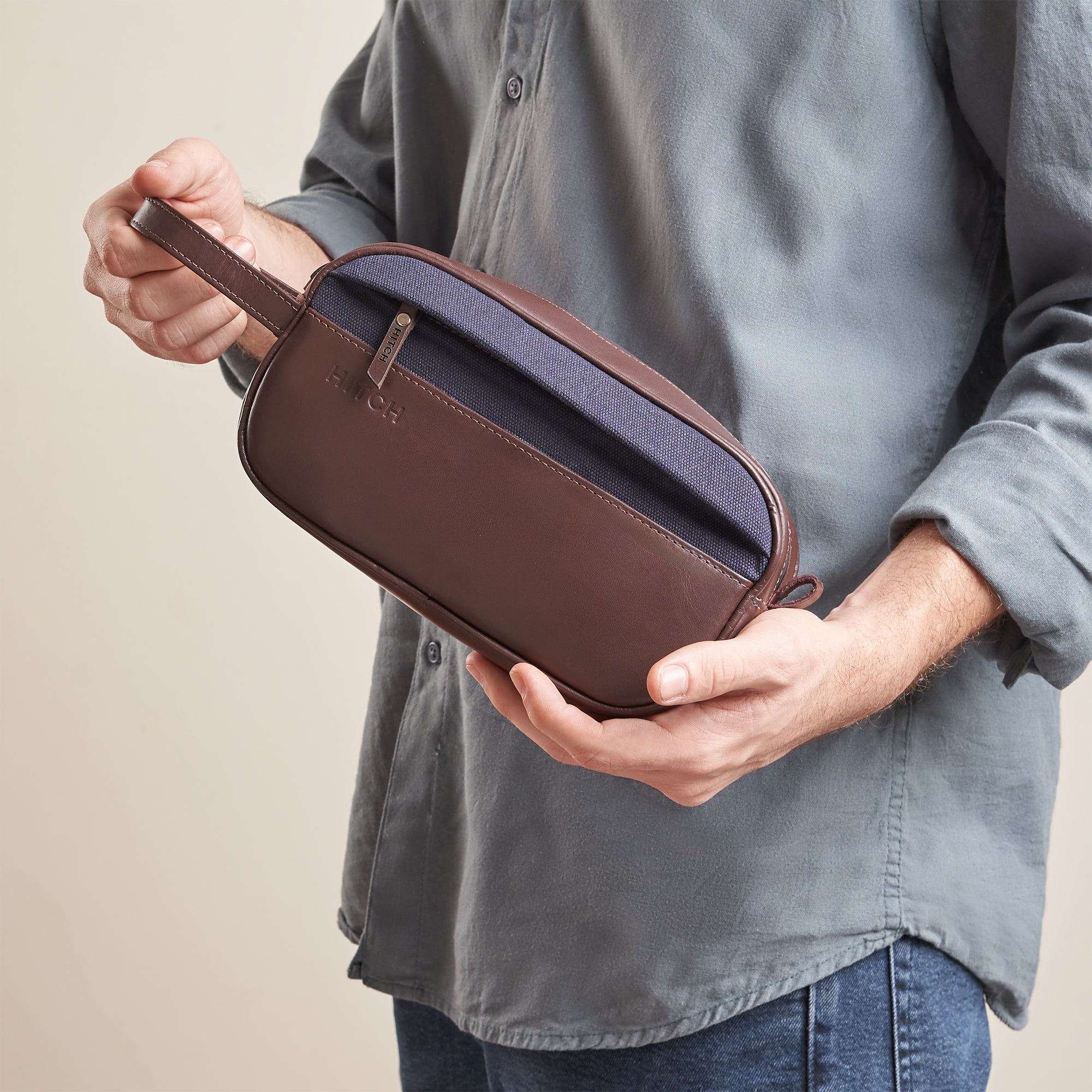 Man holding a stylish brown leather toiletry bag with zipper, casual fashion accessory.