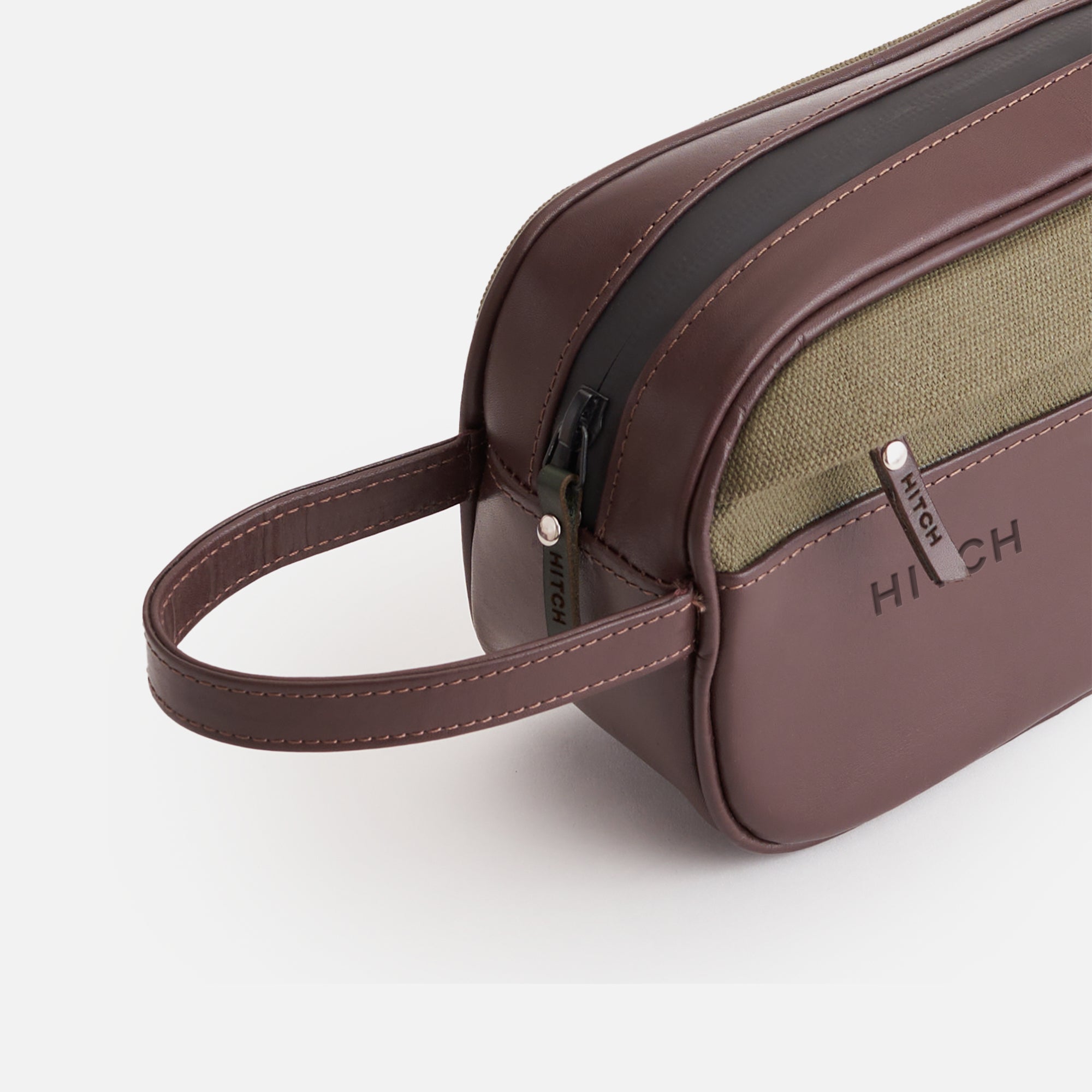 Brown and olive green designer toiletry bag with zipper and brand label "HITCH" on white background.