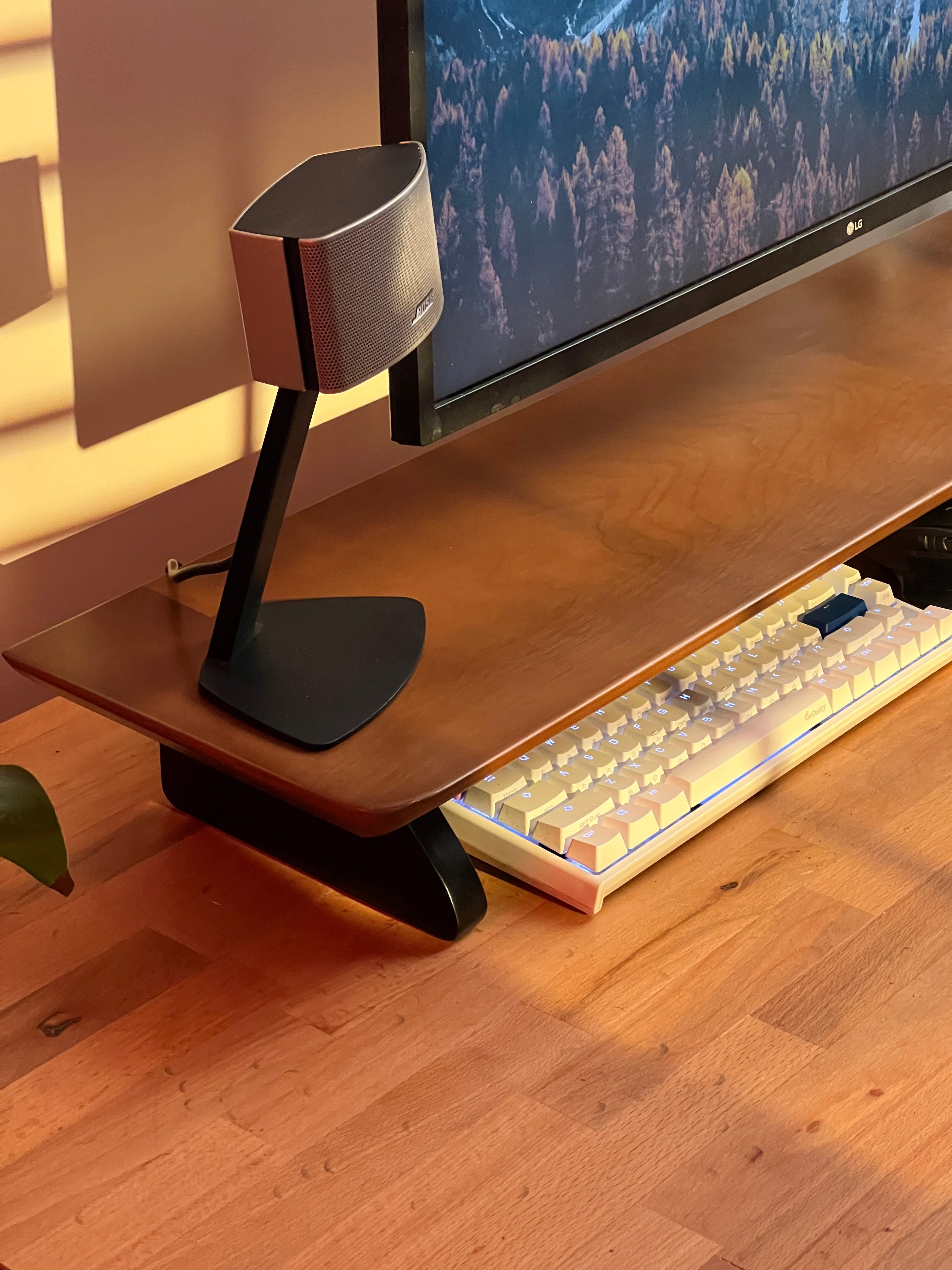 Modern workspace with stylish monitor, speaker, and mechanical keyboard on a woodsy wooden desk.