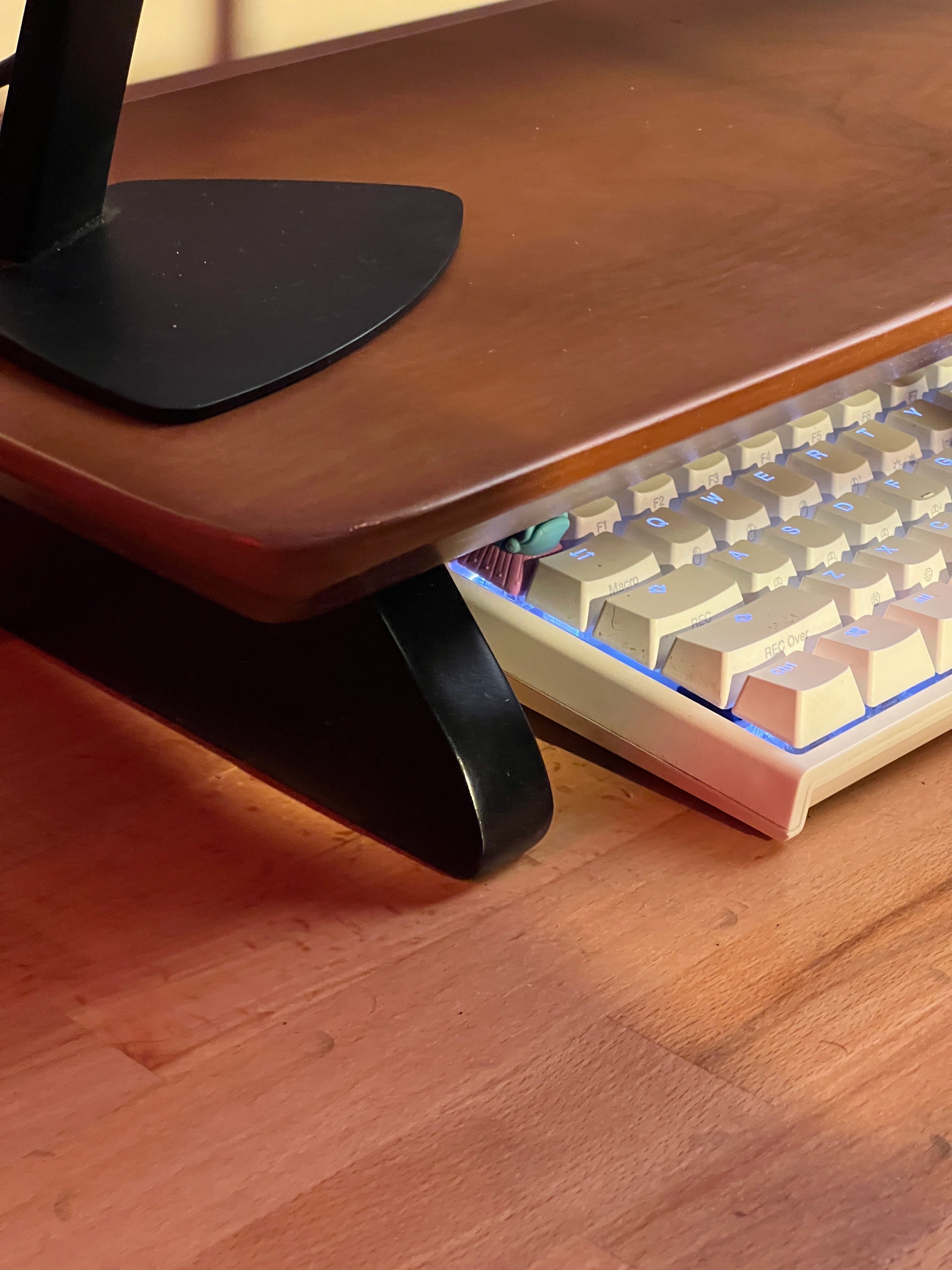 Woodsy Wooden desk with a corner of a mechanical keyboard and black monitor stand base.